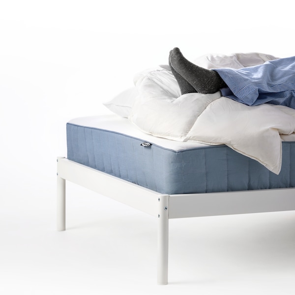 The end of a bedframe with a VESERÖY pocket spring mattress. Socked feet are propped up on a duvet on the mattress.