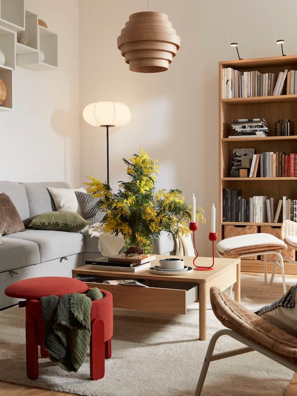 A light living room with a TONSTAD oak-veneer coffee table flanked by a BÅRSTAD sofa-bed, a red pouffe and a STOENSE rug.