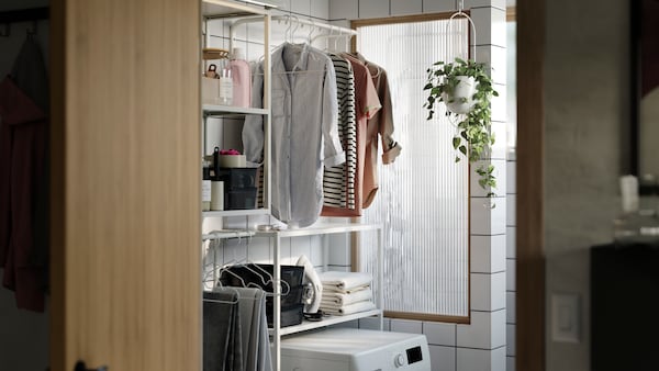 A modern laundry nook with a white ENHET frame of two shelves above and around a washing machine. Shirts hanging on a rail.