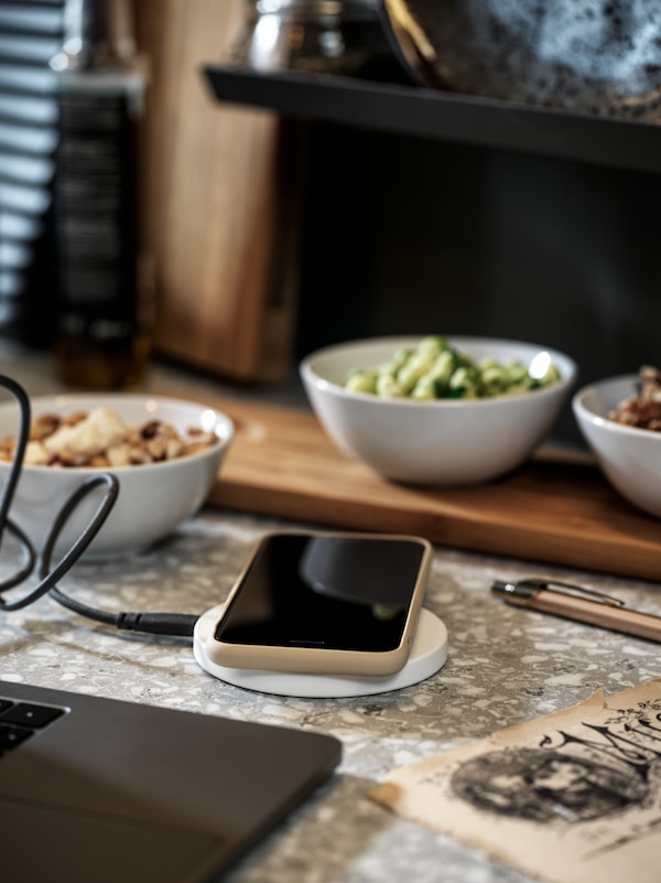 A white LIVBOJ wireless charger with a smartphone connected to it, both placed on a marble table.