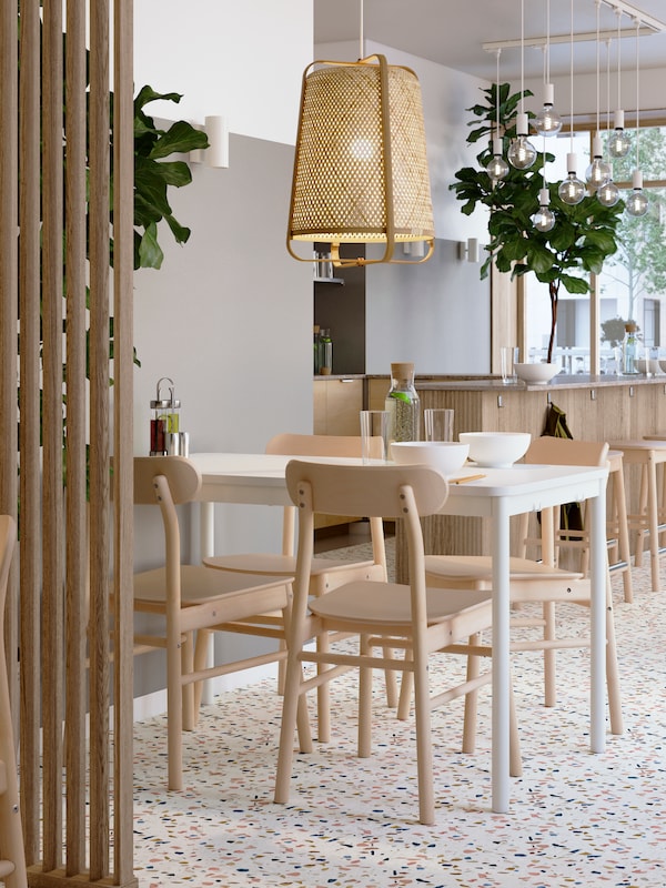 A light restaurant interior with a white TOMMARYD table and RÖNNINGE birch chairs under a KNIXHULT bamboo pendant.