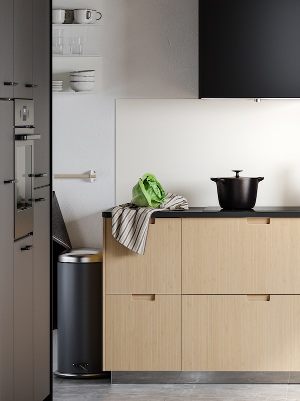 A kitchen with wooden fronts and a dark grey MJÖSA pedal bin.