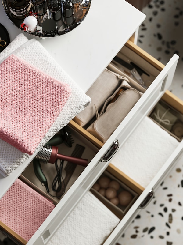 A TÄNNFORSEN wash-stand with drawers neatly organised with pink and white towels, a hairdryer, and accessories stored inside.