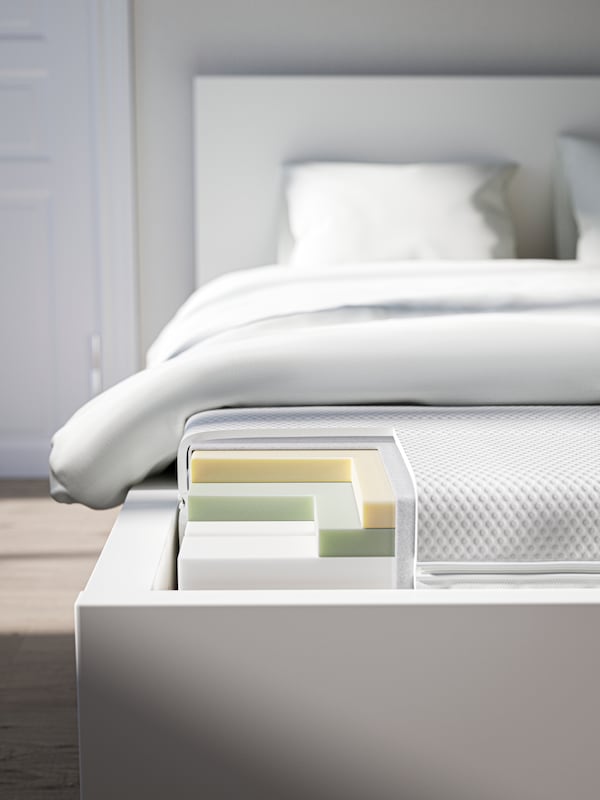 The foot end of a bed, with the corner of the foam mattress cut out to show the layers of different types of foam inside.