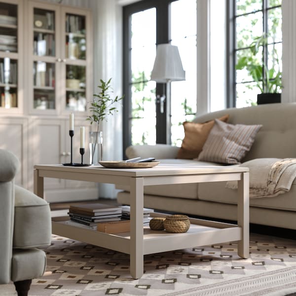 A grey-beige HAVSTA coffee table stands on a patterned rug on the floor of a living room in front of a sofa.