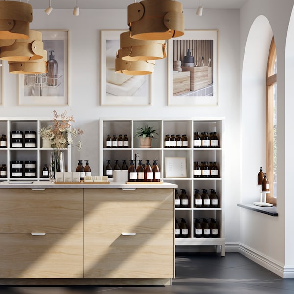 A bright, spacious store interior centred round a large kitchen island with light-ash-effect ASKERSUND drawer fronts.