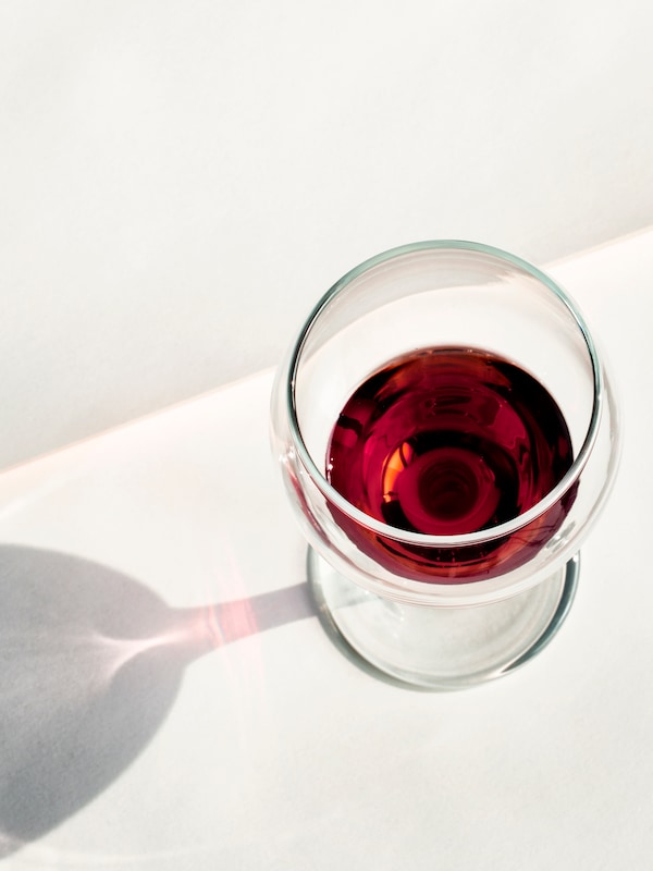 A top view of an ÄNKEBLOMSTER wine glass standing on a white surface. There is a red liquid inside the glass. 