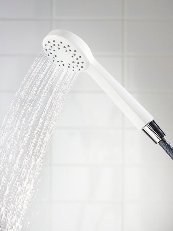 A white shower head with water flowing out of it in a white tiled bathroom.