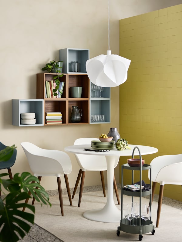 A small dining room with wall-mounted EKET shelving units in the background and a white DOCKSTA table and GRÖNSTA chairs in front.