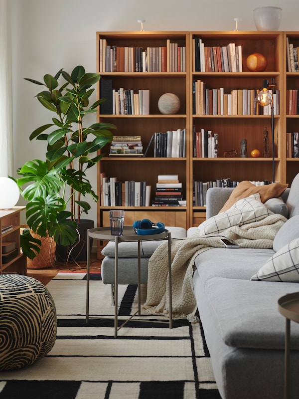 A light living room with textiles in a SÖDERHAMN sofa, TONSTAD oak-veneer bookcases, a GLADOM tray table and leafy plants.