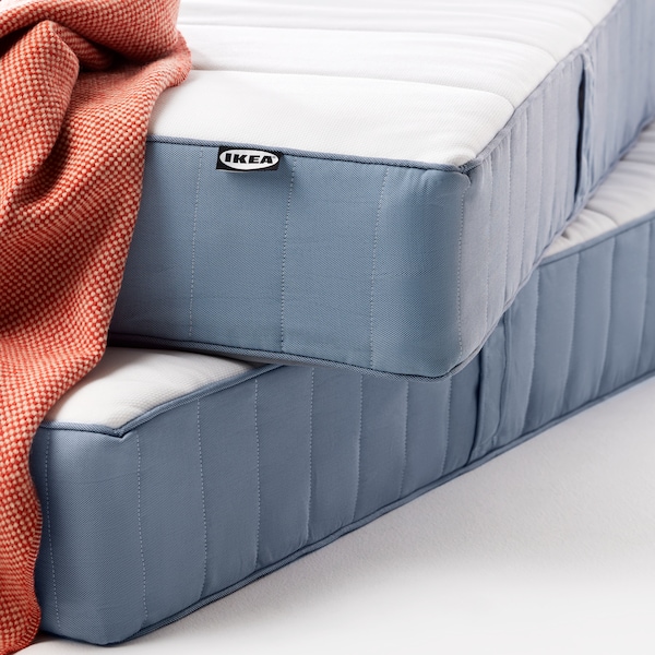 A close-up of the corners of 2 stacked VESTERÖY pocket spring mattresses with an orange throw draped over an edge.