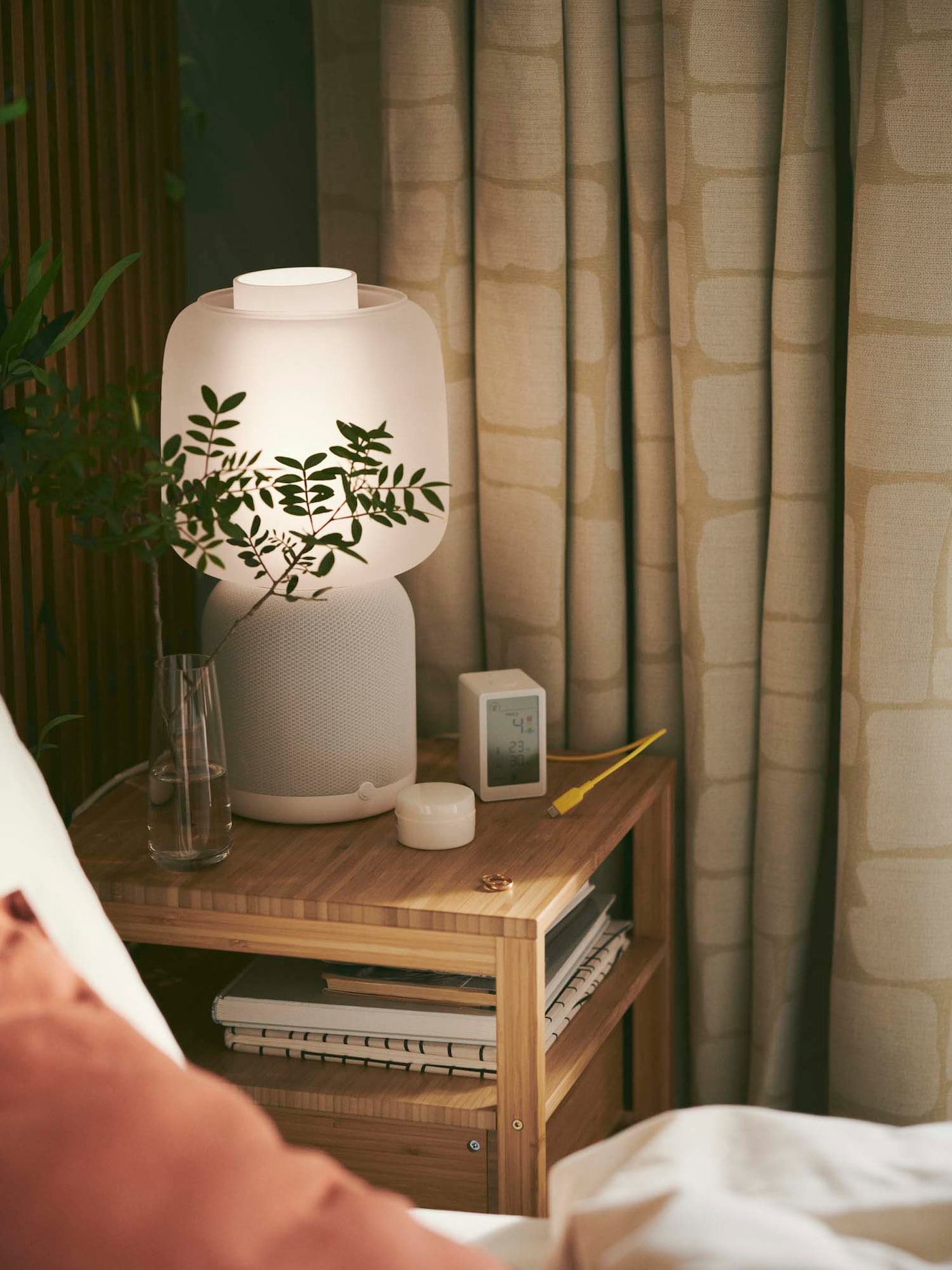 A bedside table with an illuminated SYMFONISK speaker lamp and VINDSTYRKA smart air quality sensor.