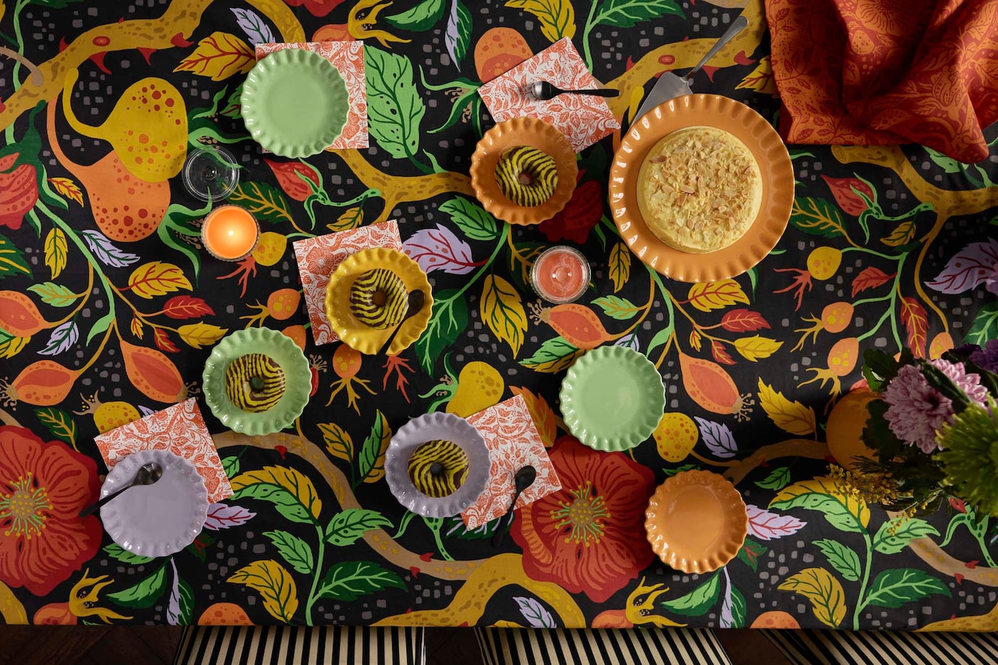 An overhead photo of a table with doughnuts on HÖSTAGILLE side plates on a multicolour HÖSTAGILLE tablecloth with botanical print.