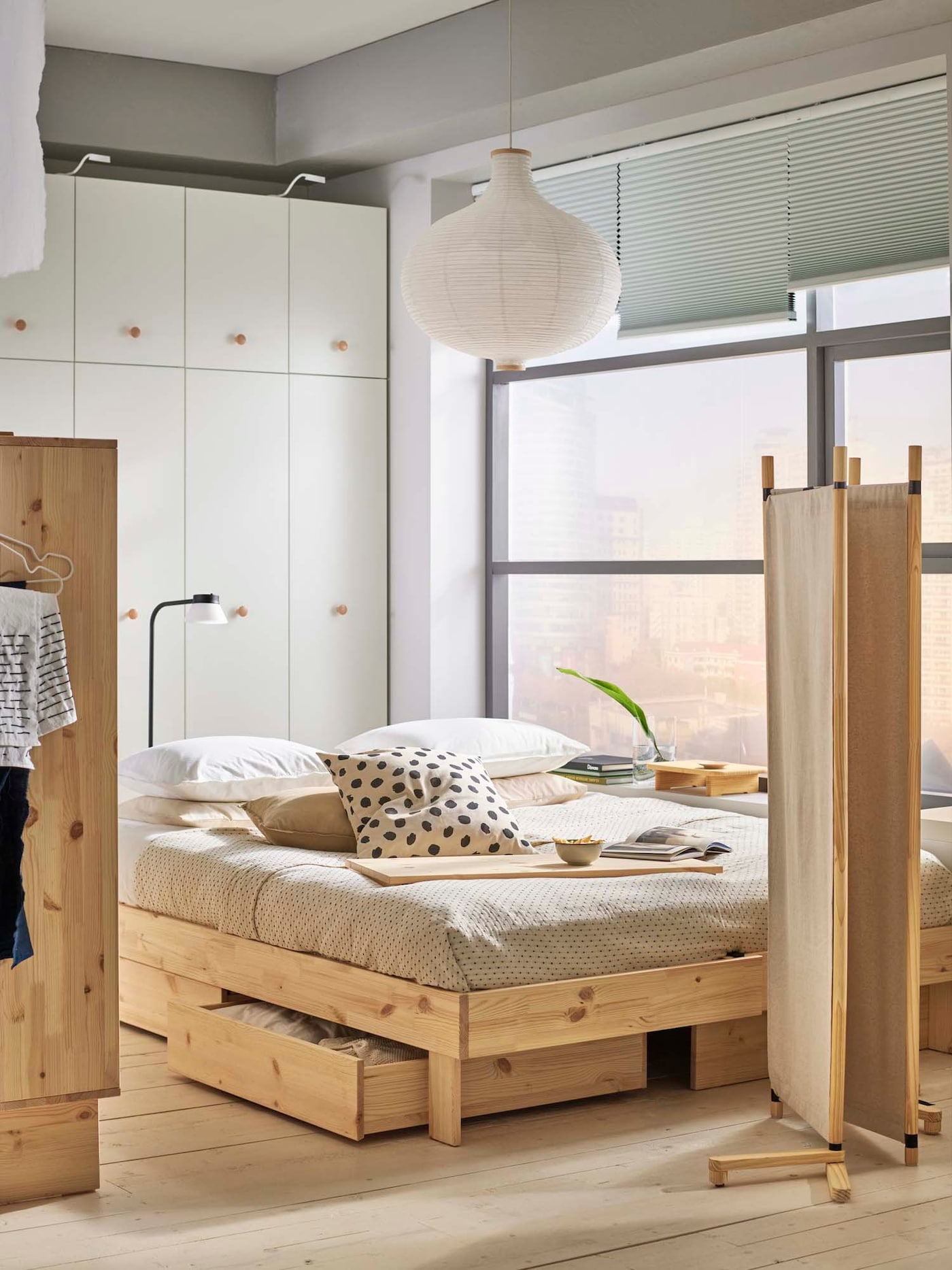 A sleeping area with a folded GLAMBERGET room divider at the foot of a pine GLAMBERGET extendable bed with storage.