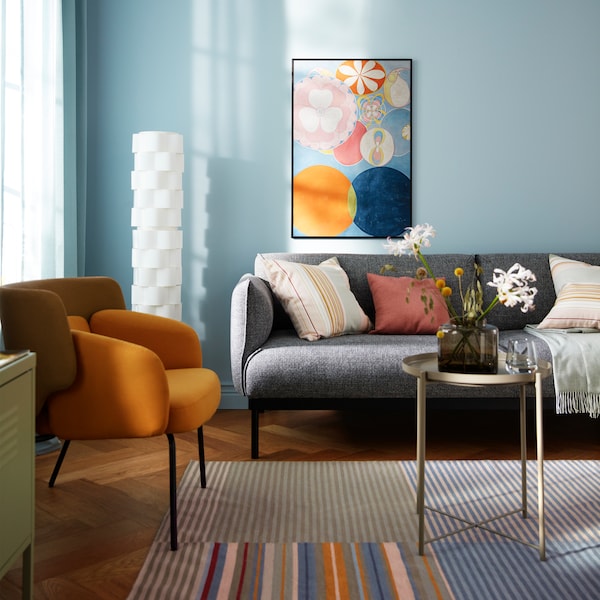 A colourful yet sparsely furnished living room with a single art piece in a black LOMVIKEN frame on a light-blue wall.