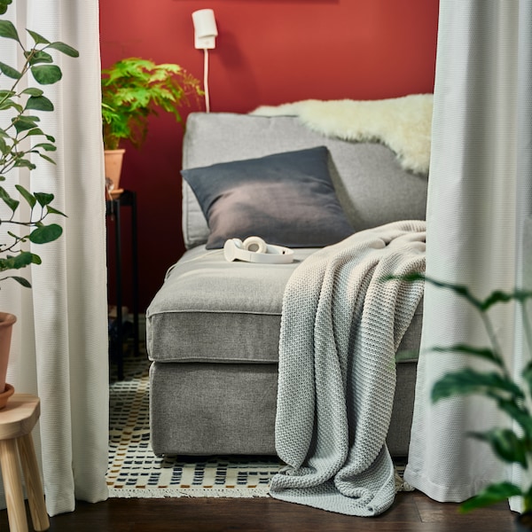 A grey KIVIK chaise longue with a light grey INGABRITTA throw and an anthracite cushion, plus a white NYMÅNE wall lamp.