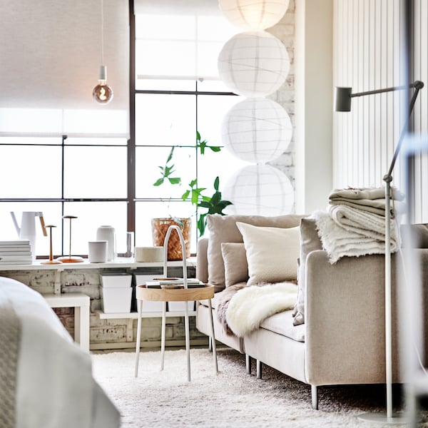 A light beige SÖDERHAMN sofa stands in a modern living room with large windows and a mostly white colour palette.