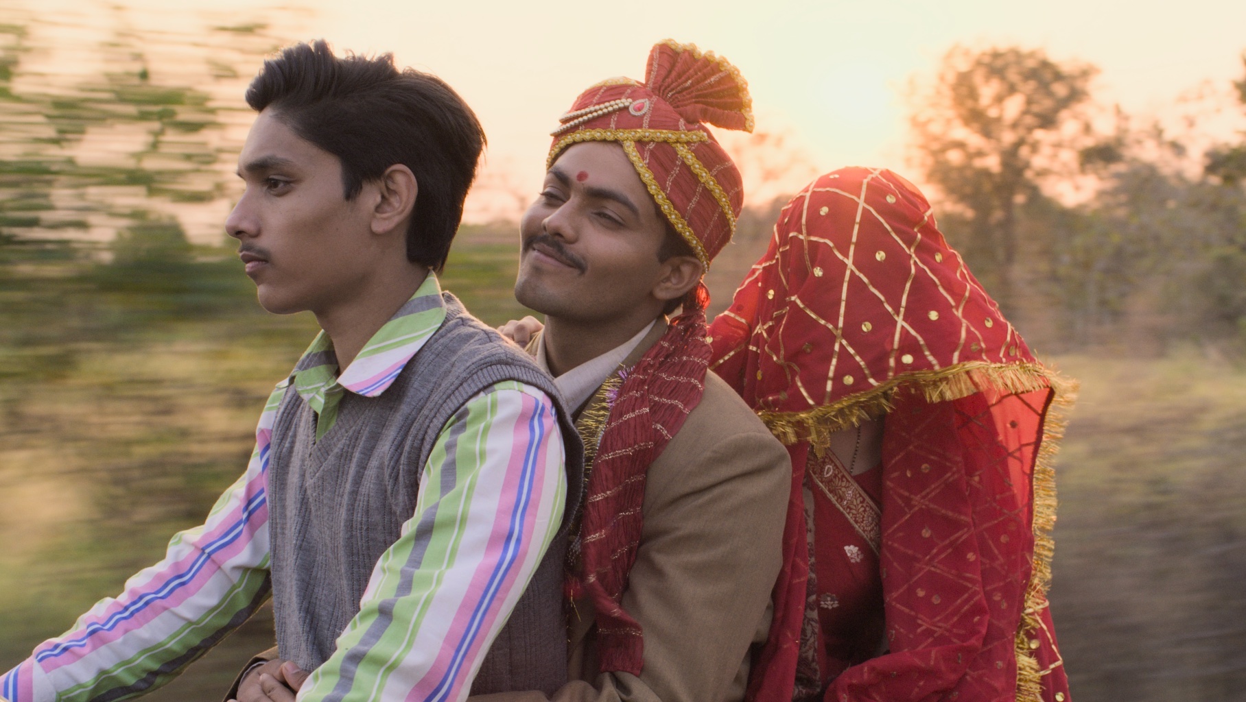 A Hindu groom and bride (her head covered with a red dupatta) and third man seated against a moving background, on a scooter; still from 'Lost Ladies'