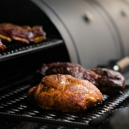 Closeup of chef cooking poultry, beef and pork meat, ribs in BBQ smoker