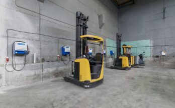 A warehouse storage area with a few forklifts parked off to the sides. There are chargers mounted on the wall.