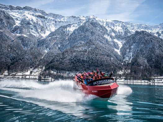 Jetboat unterwegs auf dem spiegelglatten Brienzersee im Winter mit verschneiten Wälder und Bergen