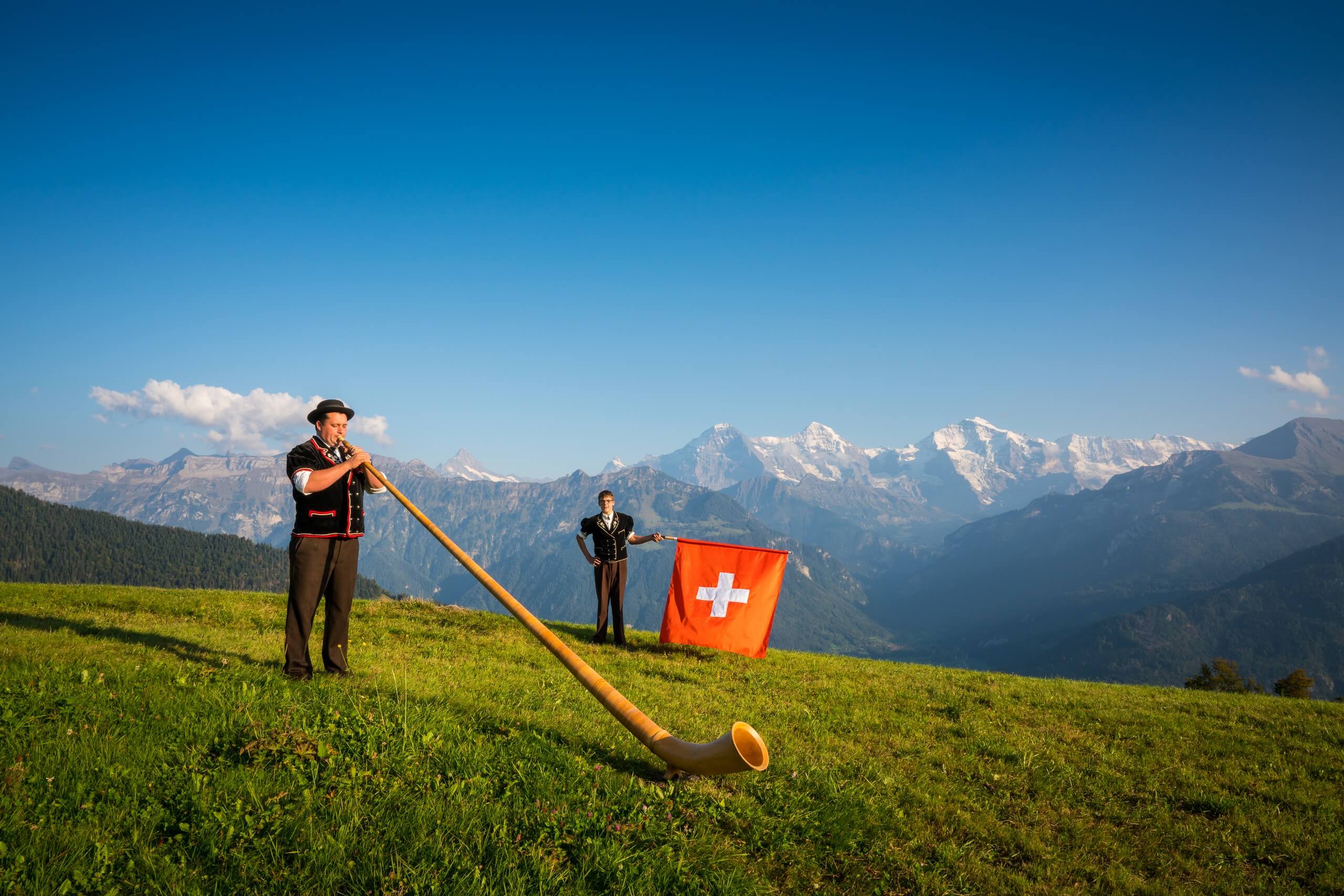 Ein Fahnenschwinger und ein Alphornbläser posieren auf Amisbühl bei Beatenberg vor Eiger, Mönch und Jungfrau