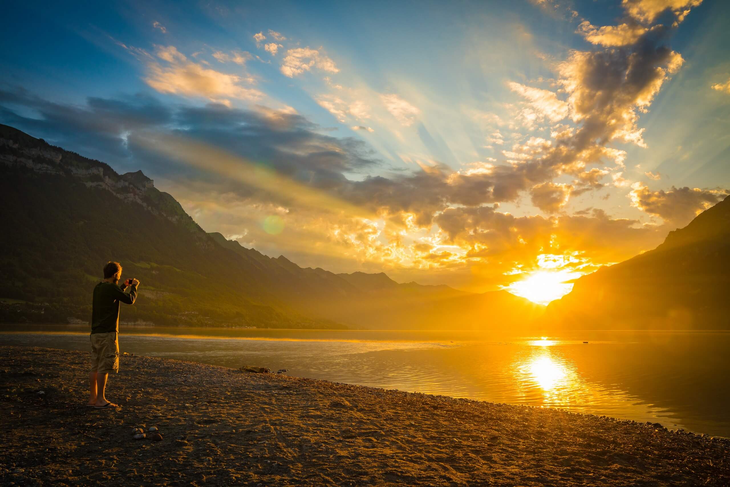 Ein Spaziergänger fotografiert den Sonnenaufgang am Brienzersee.