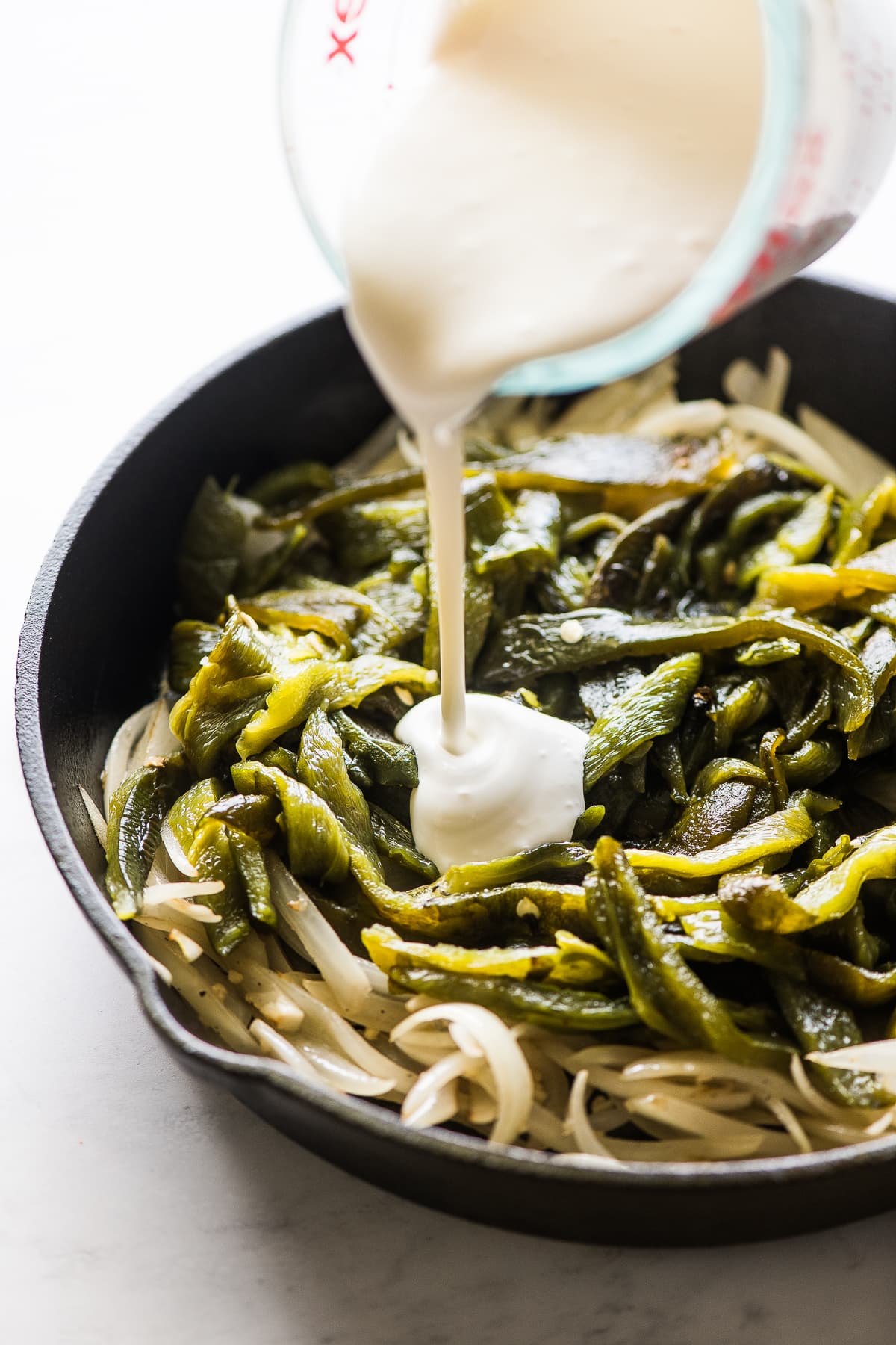 Crema mexicana a ser vertida em cima de poblanos e cebolas.