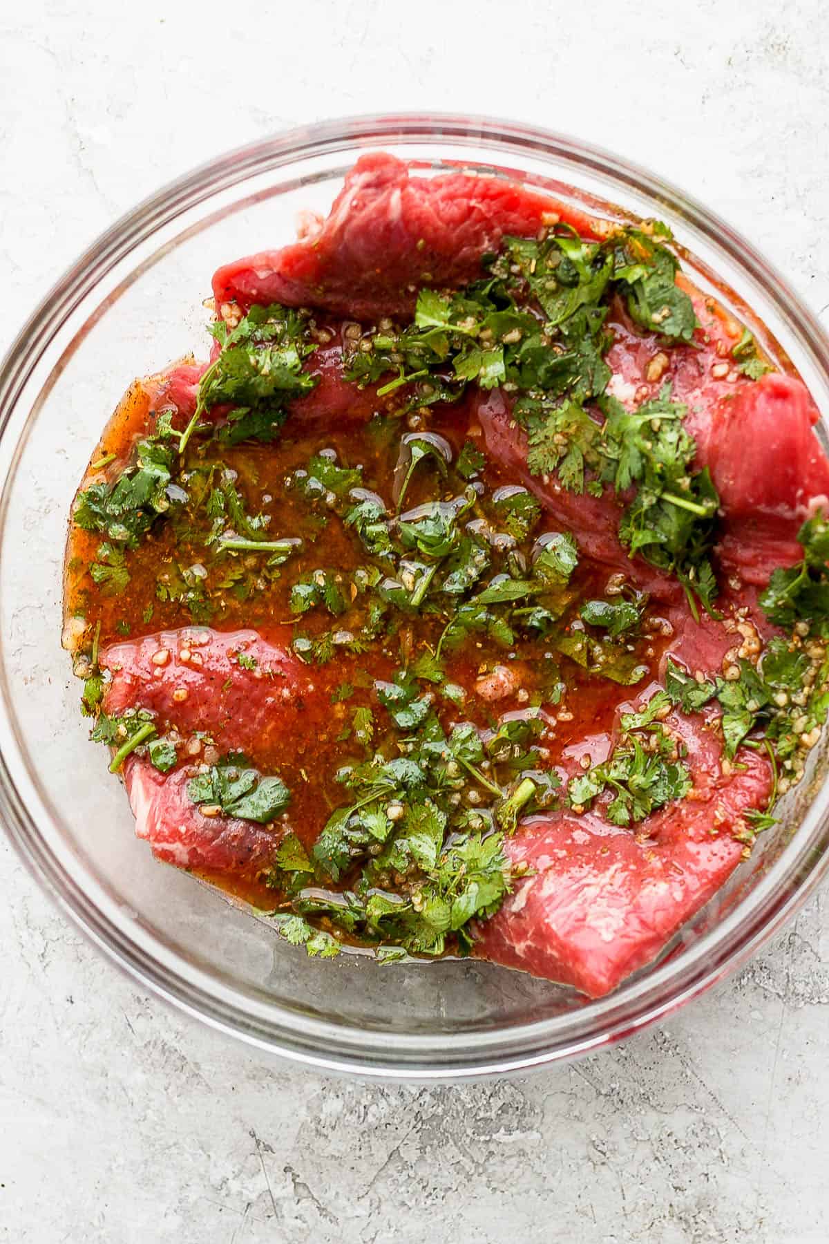 Raw flank steak marinating in a bowl.