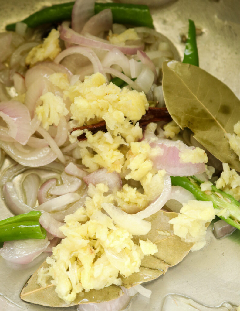 adding minced ginger to the cooking onions, bay leaves and spices.