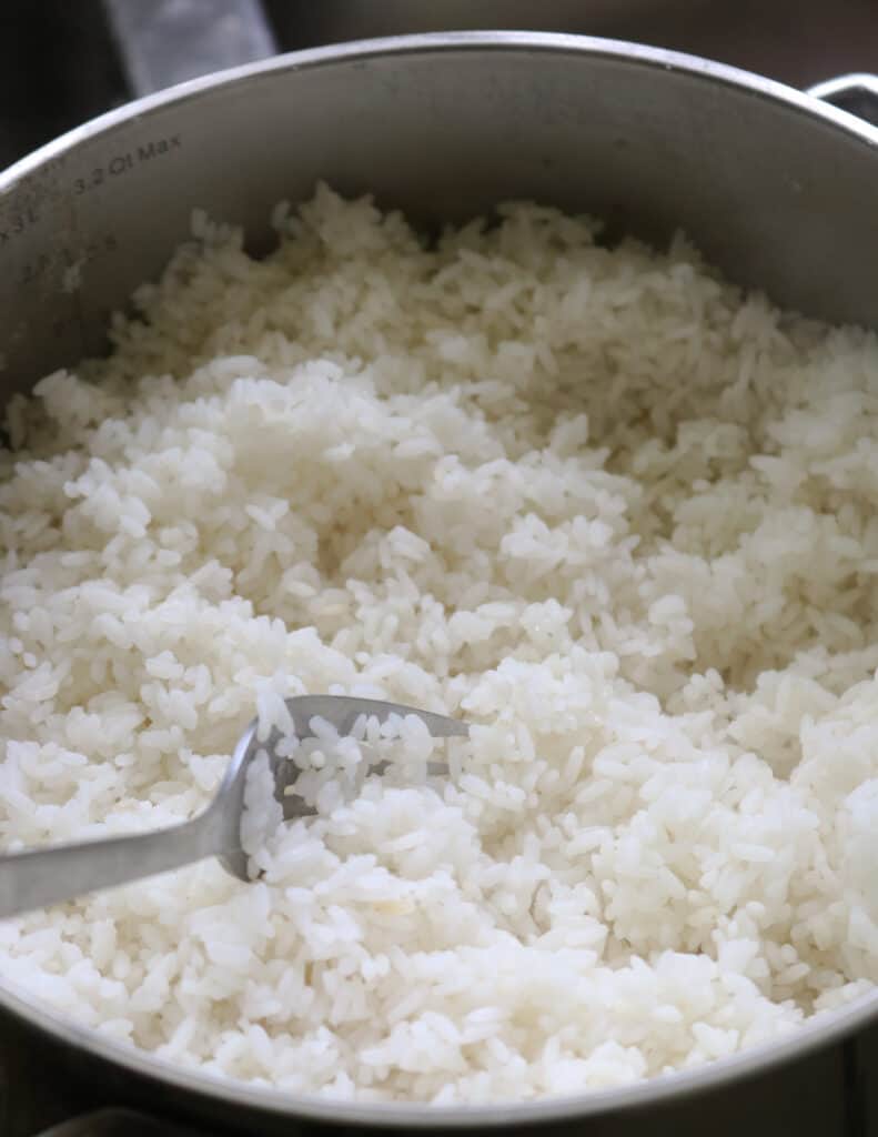 fluffing the rice cooked over a stove top with a fork.