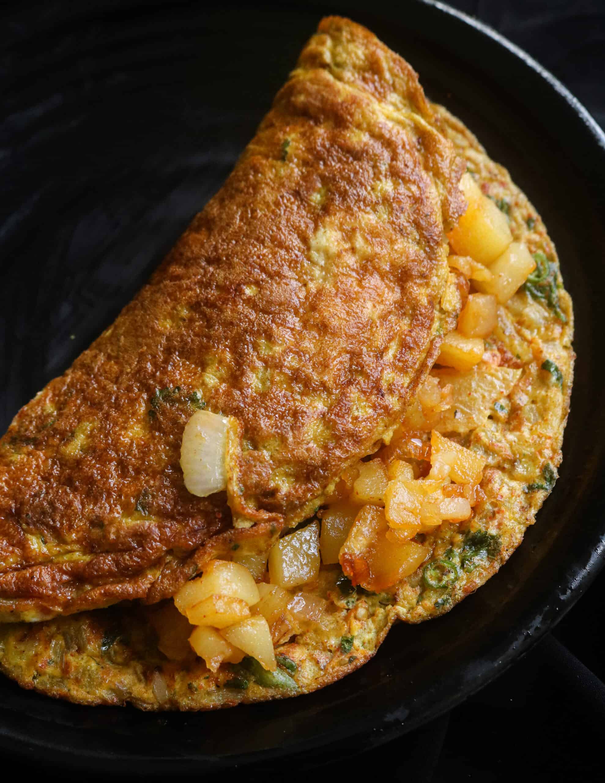 cooked masala omelette with crispy fried potatoes stuffed into it.