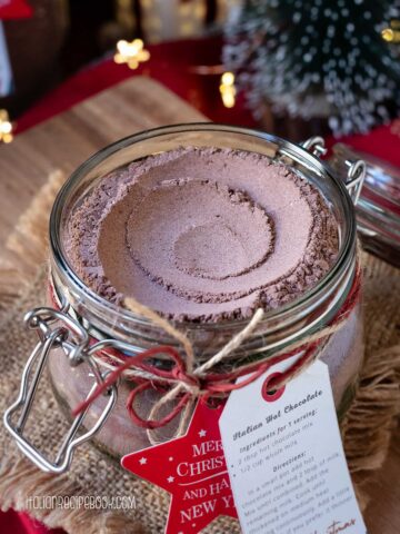 Homemade hot chocolate mix in a glass jar with Christmas decorations in the background.