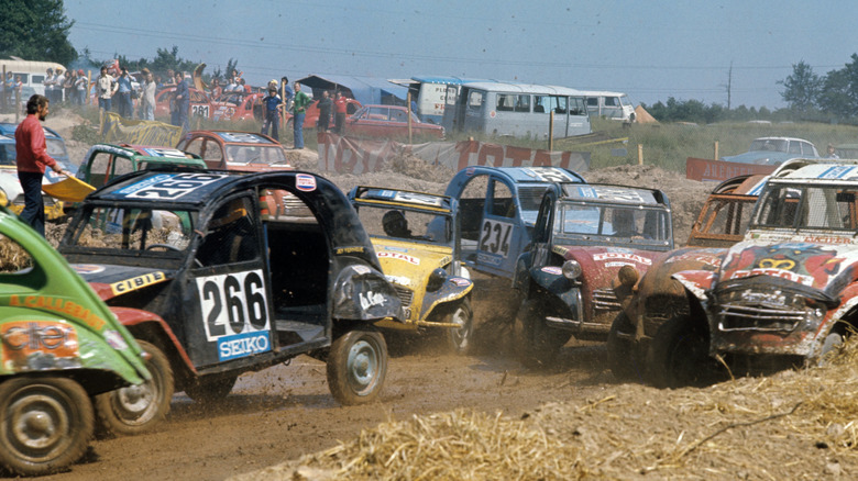 A pack of stripped down Citroen 2CVs on a muddy dirt track during a 24-hour endurance race in 1975