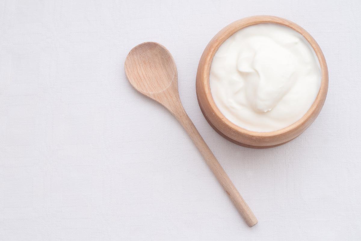 plain yoghurt in a wooden bowl next to a wooden spoon