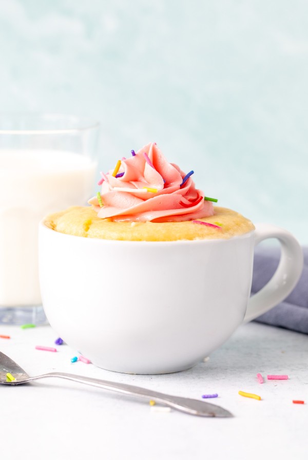 Vanilla mug cake decorated with pink frosting with a glass of milk