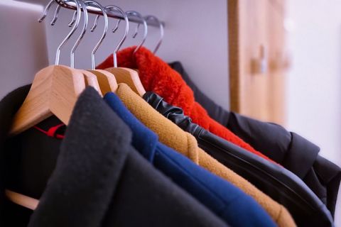 Eine Reihe Wintermäntel in verschiedenen Farben, darunter Schwarz, Blau, Braun und Rot, hängen ordentlich auf Holzbügeln in einem Kleiderschrank.