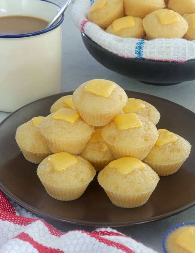 Cheese Puto on a brown serving plate with cup of coffee in the background.