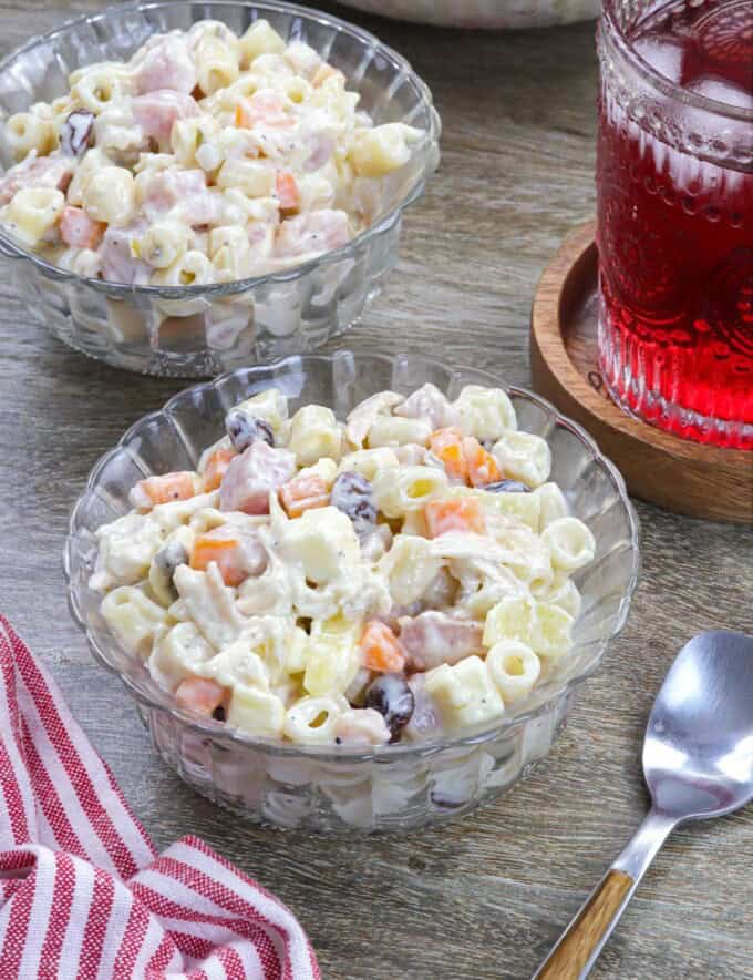 Macaroni Ham Salad in a bowl with a glass of juice in the background.