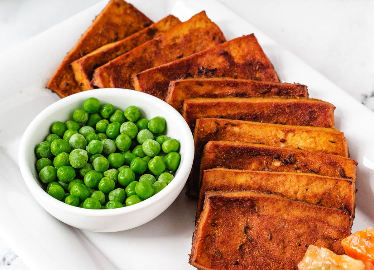 Tofu vegan corned beef slices on serving plate with a side of peas.