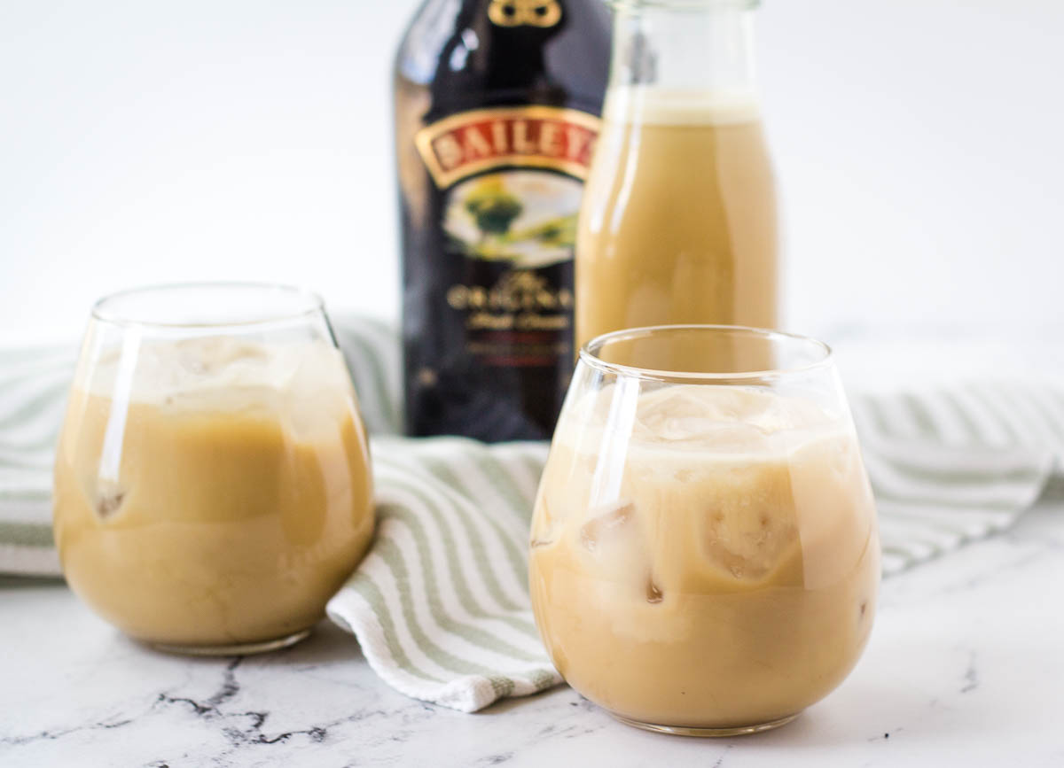 Vegan Irish cream in two stemless wine glasses with Bailey's bottle in the background.