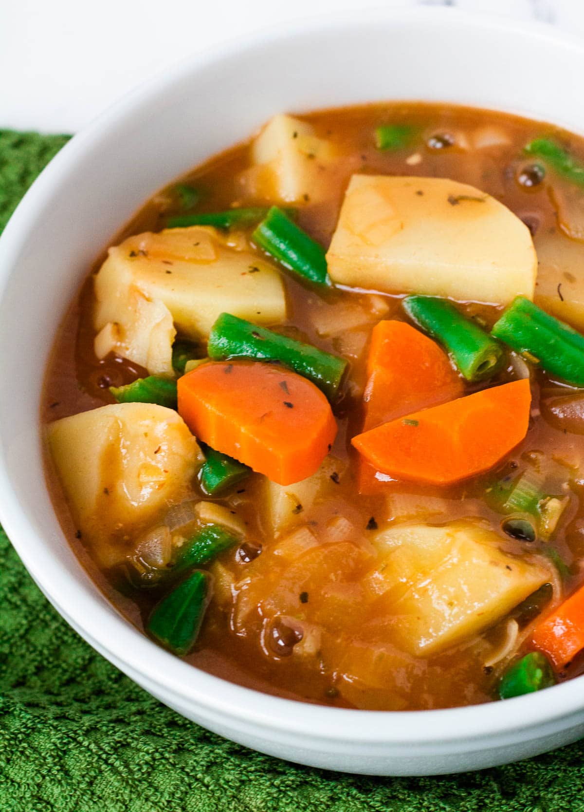 Vegan Irish stew in white bowl with carrots, potatoes, and green beans.