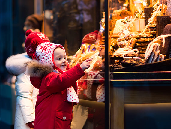 A child dressed in a winter coat and woolen hat, pointing into the window of a bakery