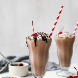 a large glass with a chocolate milkshake topped with whipped cream, sprinkles and a cherry