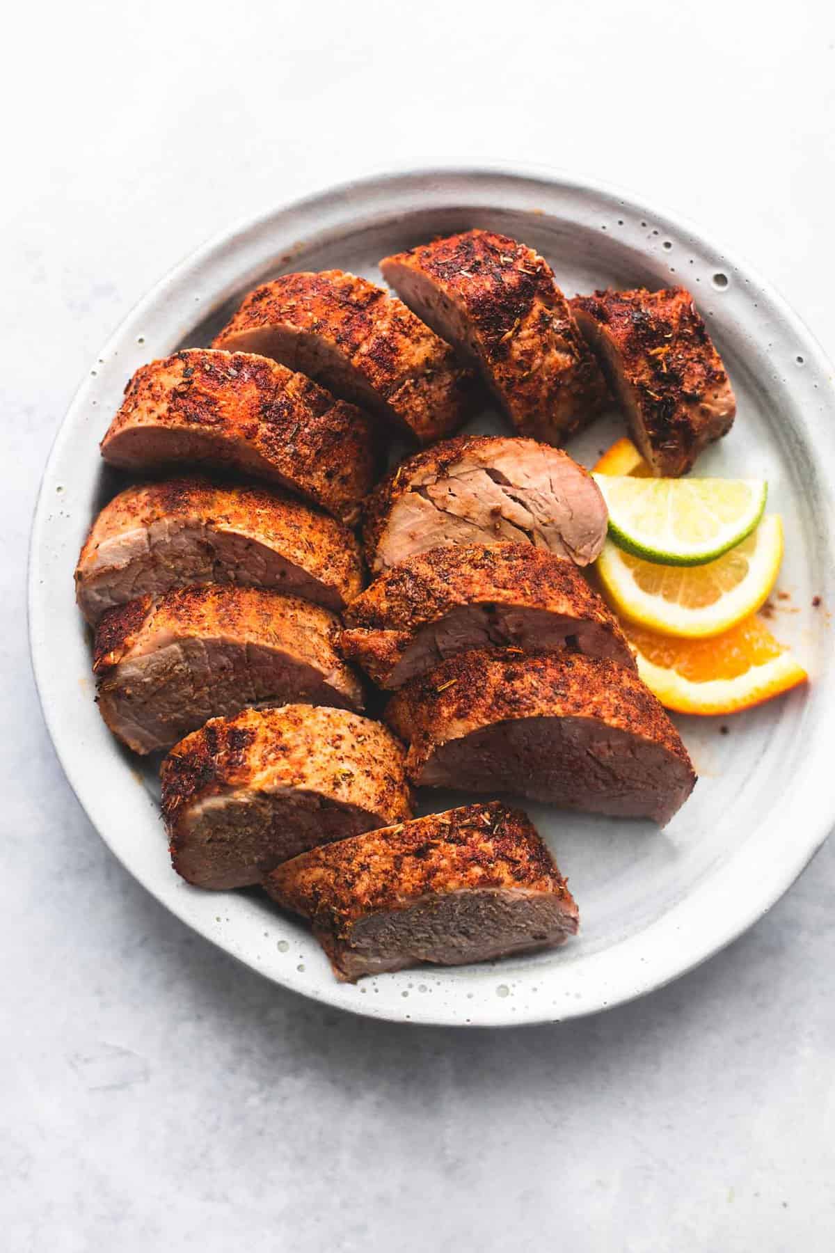 sliced pork tenderloin on a plate with lemon, lime, and orange slices