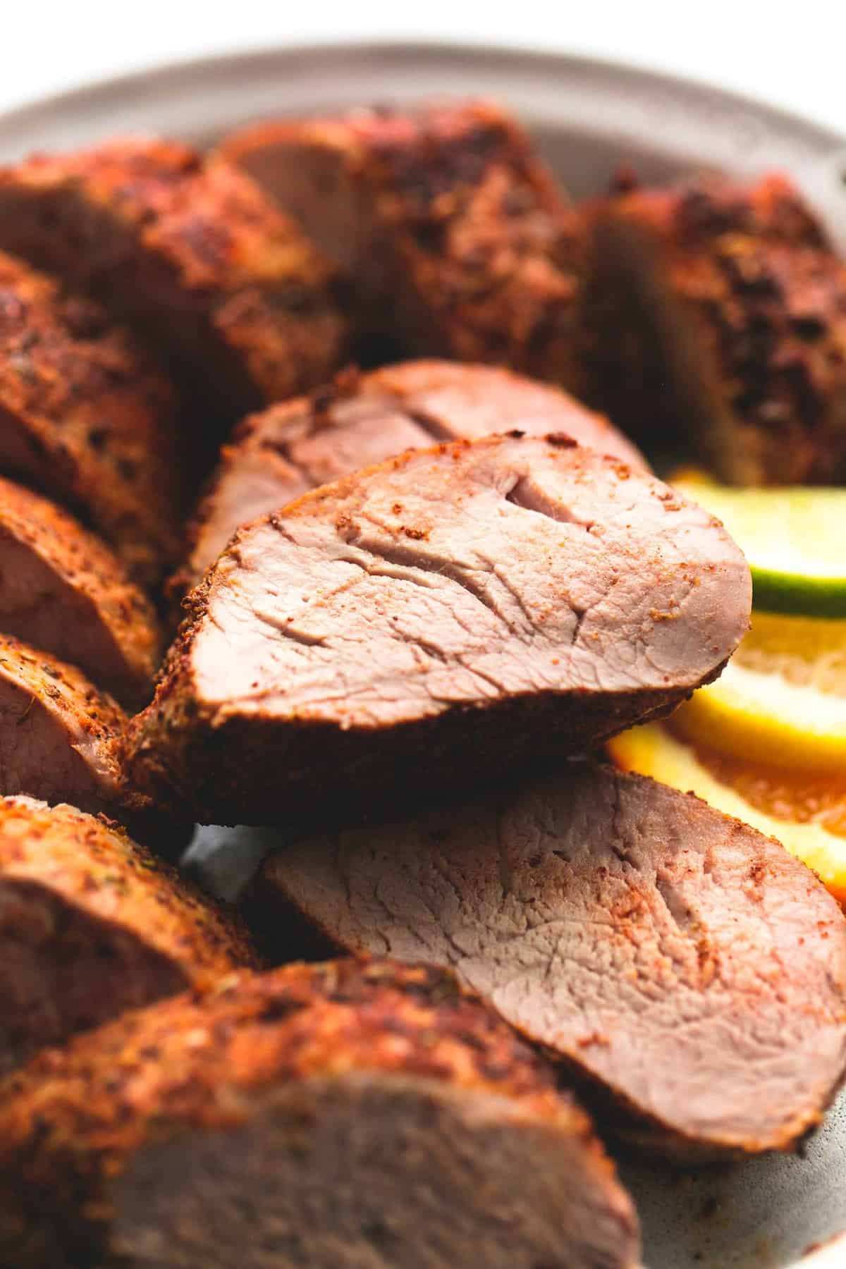 Up close sliced pork tenderloin on a plate with lemon, lime, and orange slices