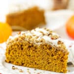 A slice of pumpkin coffee cake on a plate with a second slice and a jar of cinnamon sticks in the background