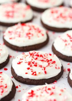 Several Peppermint Frosted Chocolate Cookies topped with candy cane bits on a flat surface.