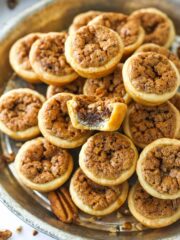 A metal tray full of pecan tassies with a bite missing from the top one.