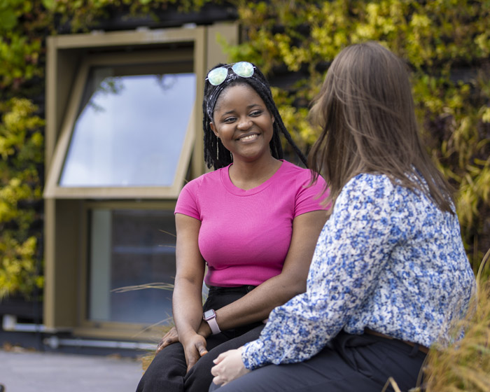 Tow students sitting chatting in front of a campus building